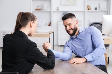 Photo of Businesspeople arm wrestling at wooden table in office
