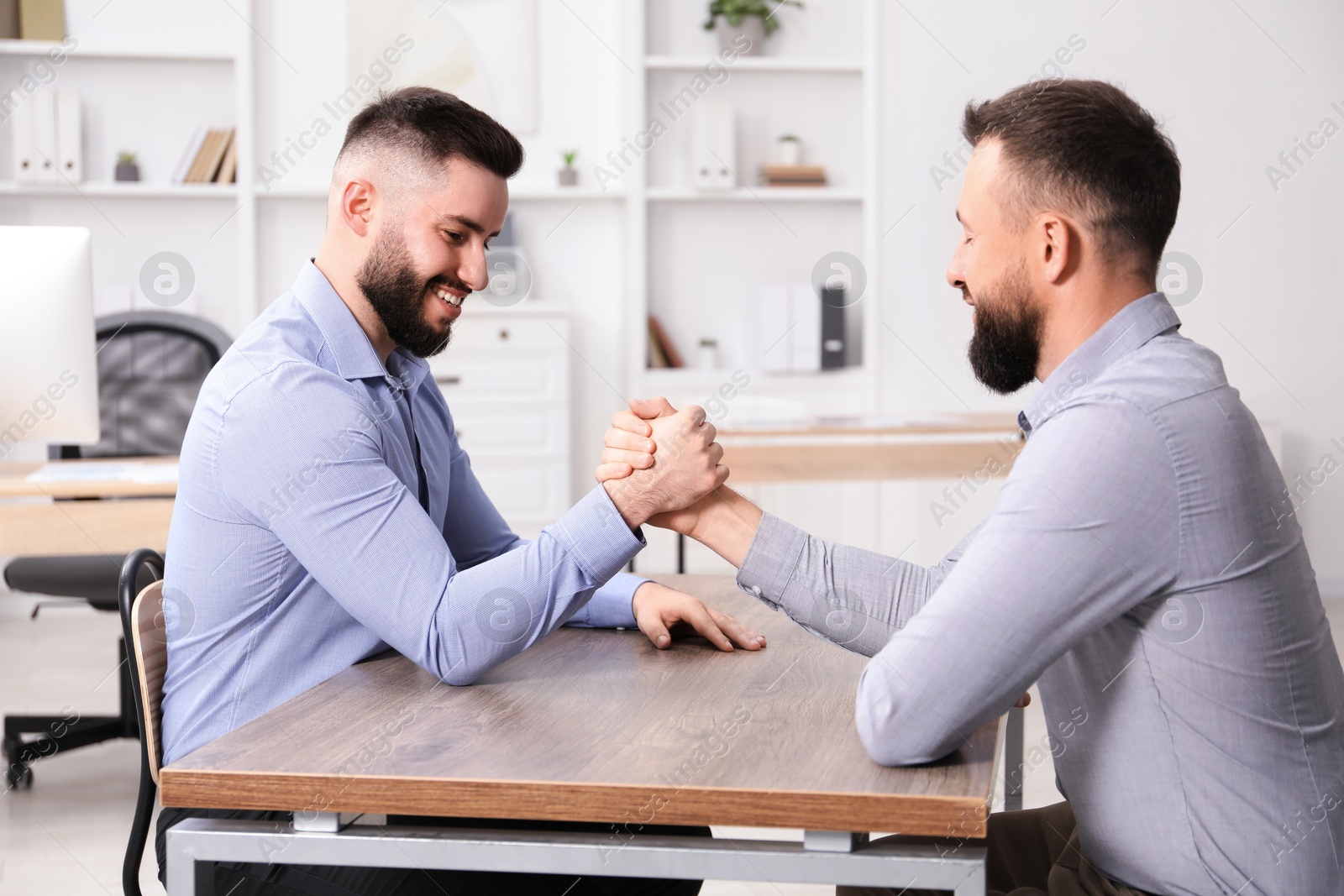 Businessmen arm wrestling at wooden table in office Photo of Businessmen arm wrestling at wooden table in office