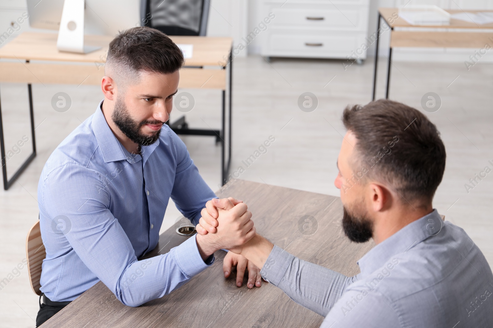 Businessmen arm wrestling at wooden table in office Photo of Businessmen arm wrestling at wooden table in office