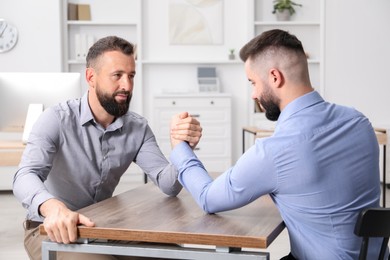 Photo of Businessmen arm wrestling at wooden table in office