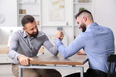 Photo of Businessmen arm wrestling at wooden table in office