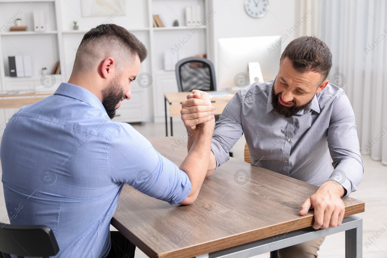 Businessmen arm wrestling at wooden table in office Photo of Businessmen arm wrestling at wooden table in office