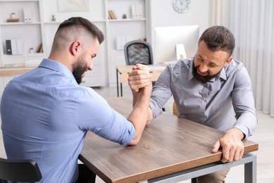 Photo of Businessmen arm wrestling at wooden table in office