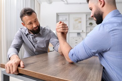 Photo of Businessmen arm wrestling at wooden table in office