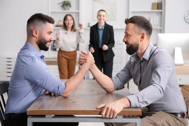 Photo of Businessmen arm wrestling at table in office, selective focus