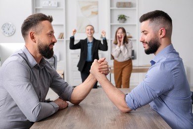 Photo of Businessmen arm wrestling at table in office, selective focus