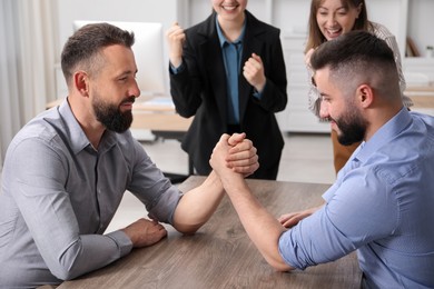Photo of Businesspeople arm wrestling at wooden table in office