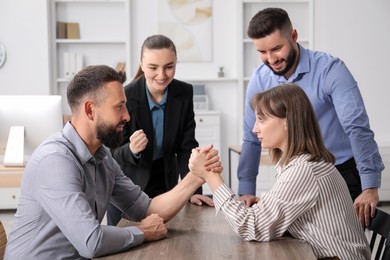 Photo of Businesspeople arm wrestling at wooden table in office
