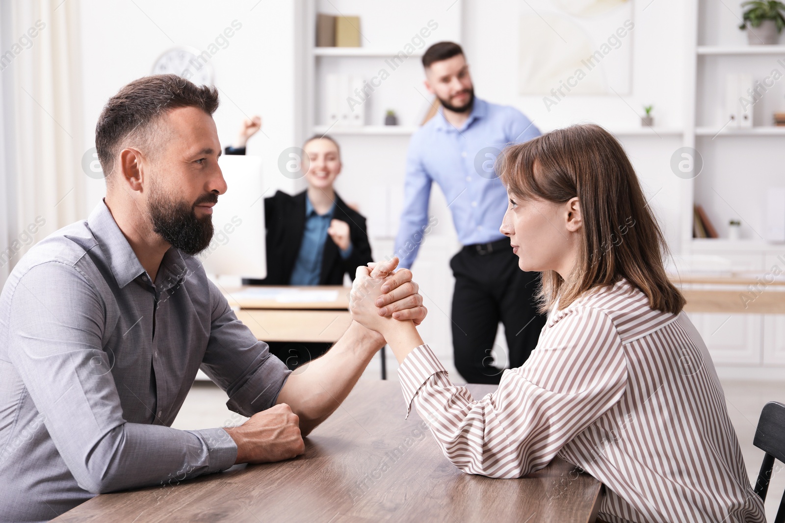 Businesspeople arm wrestling at wooden table in office, selective focus Photo of Businesspeople arm wrestling at wooden table in office, selective focus
