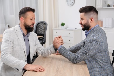 Photo of Businessmen arm wrestling at wooden table in office