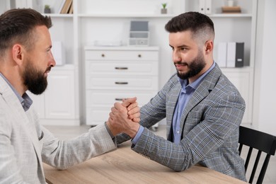 Photo of Businessmen arm wrestling at wooden table in office