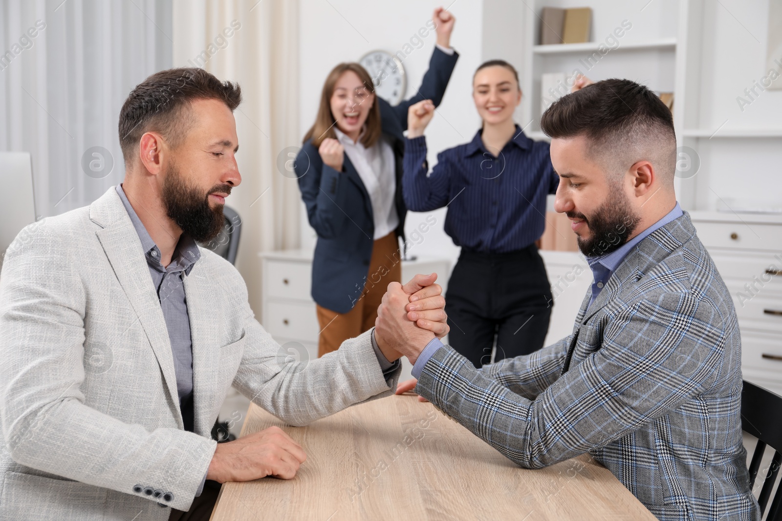 Businessmen arm wrestling at wooden table in office, selective focus Photo of Businessmen arm wrestling at wooden table in office, selective focus