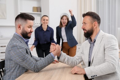 Photo of Businessmen arm wrestling at wooden table in office, selective focus