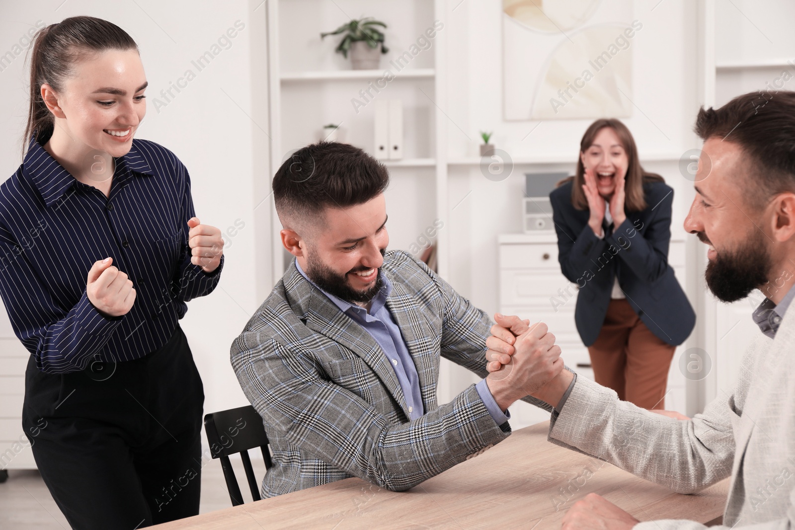 Businessmen arm wrestling at wooden table in office Photo of Businessmen arm wrestling at wooden table in office