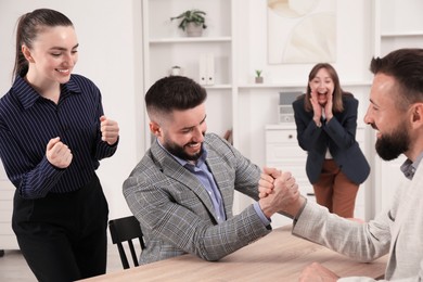 Photo of Businessmen arm wrestling at wooden table in office