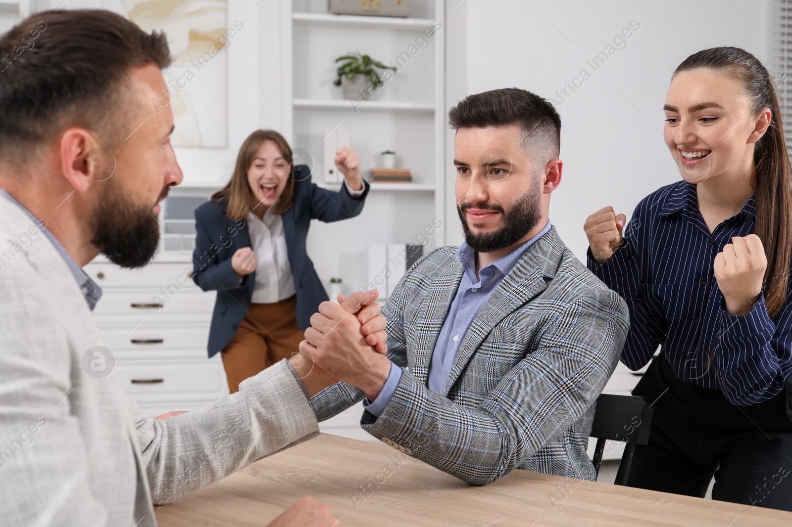 Businessmen arm wrestling at wooden table in office Photo of Businessmen arm wrestling at wooden table in office