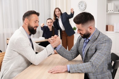 Photo of Businessmen arm wrestling at wooden table in office, selective focus