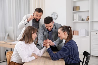 Photo of Businesswomen arm wrestling at wooden table in office