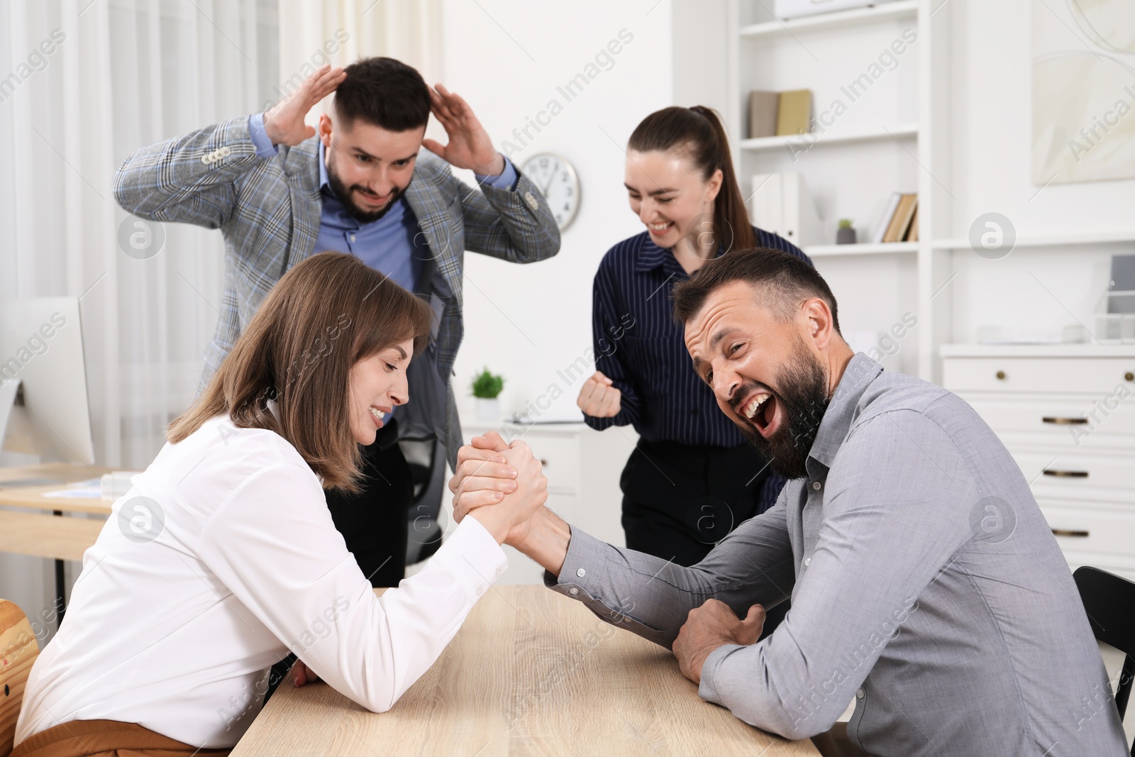Businesspeople arm wrestling at wooden table in office Photo of Businesspeople arm wrestling at wooden table in office