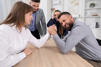 Photo of Businesspeople arm wrestling at wooden table in office