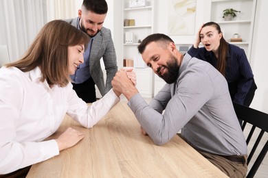 Photo of Businesspeople arm wrestling at wooden table in office