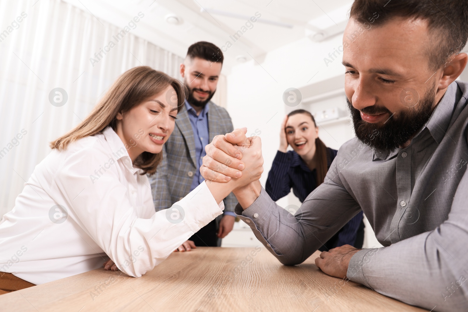Businesspeople arm wrestling at wooden table in office Photo of Businesspeople arm wrestling at wooden table in office