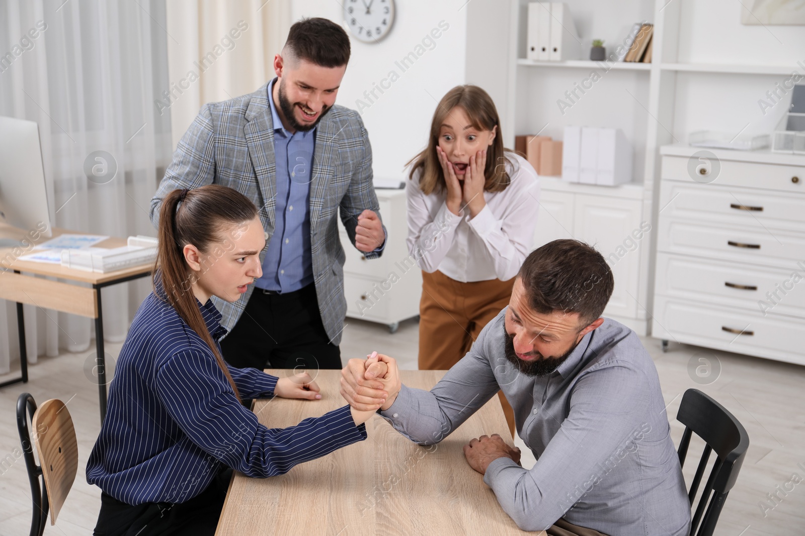 Businesspeople arm wrestling at wooden table in office Photo of Businesspeople arm wrestling at wooden table in office