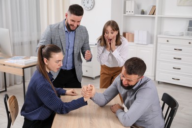 Photo of Businesspeople arm wrestling at wooden table in office