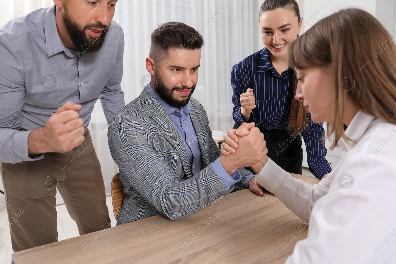 Businesspeople arm wrestling at wooden table in office Photo of Businesspeople arm wrestling at wooden table in office