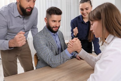 Photo of Businesspeople arm wrestling at wooden table in office