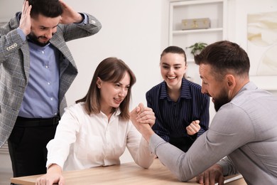 Photo of Businesspeople arm wrestling at wooden table in office