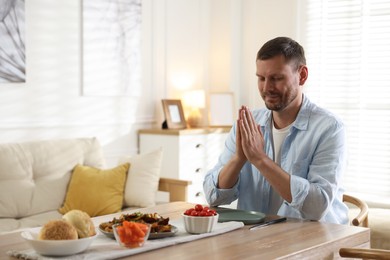 Photo of Man praying before dinner at table indoors. Space for text