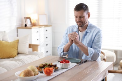 Photo of Man praying before dinner at table indoors. Space for text