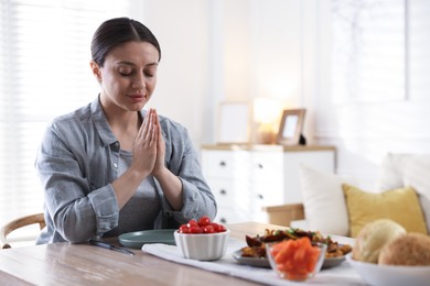 Photo of Woman praying before dinner at table indoors. Space for text