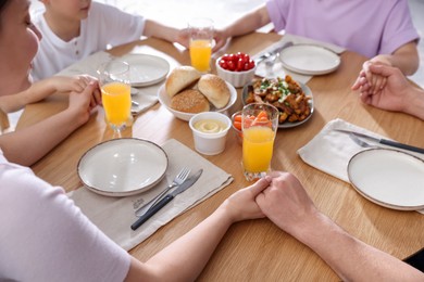 Photo of Family praying together before dinner at table indoors, closeup