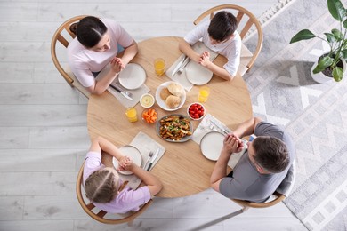 Photo of Family praying together before dinner at table indoors, above view