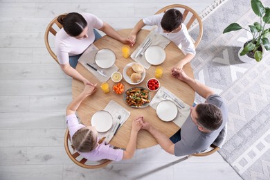Photo of Family praying together before dinner at table indoors, above view
