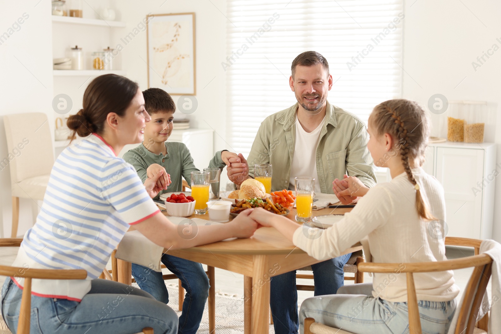 Family praying together before dinner at table indoors Photo of Family praying together before dinner at table indoors