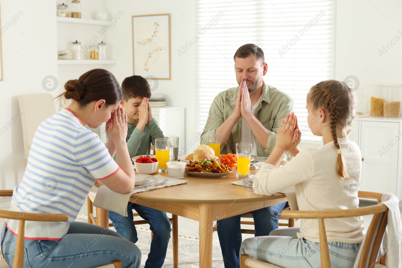 Family praying together before dinner at table indoors Photo of Family praying together before dinner at table indoors