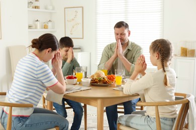 Photo of Family praying together before dinner at table indoors
