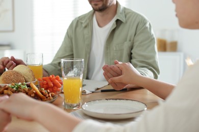 Photo of Family praying together before dinner at table indoors, closeup