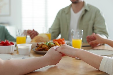 Photo of Family praying together before dinner at table indoors, closeup