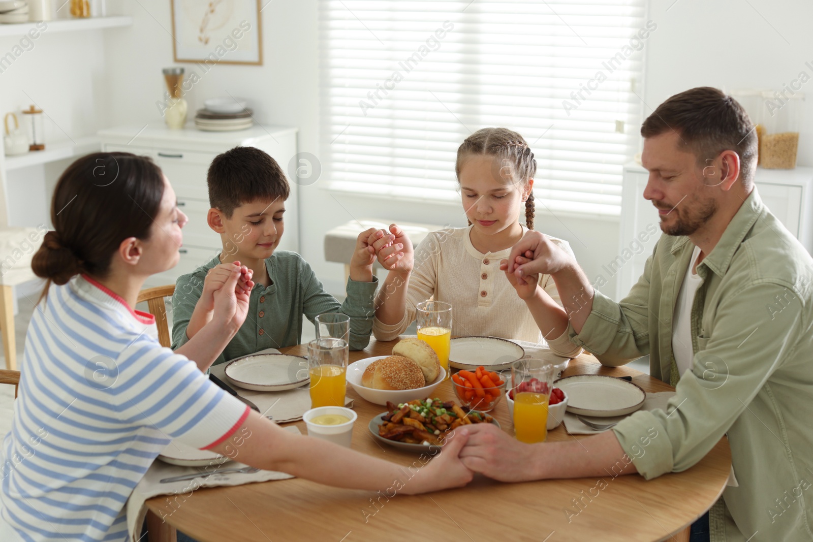 Family praying together before dinner at table indoors Photo of Family praying together before dinner at table indoors