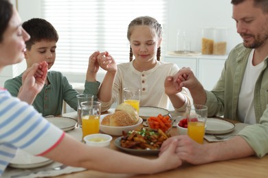 Photo of Family praying together before dinner at table indoors