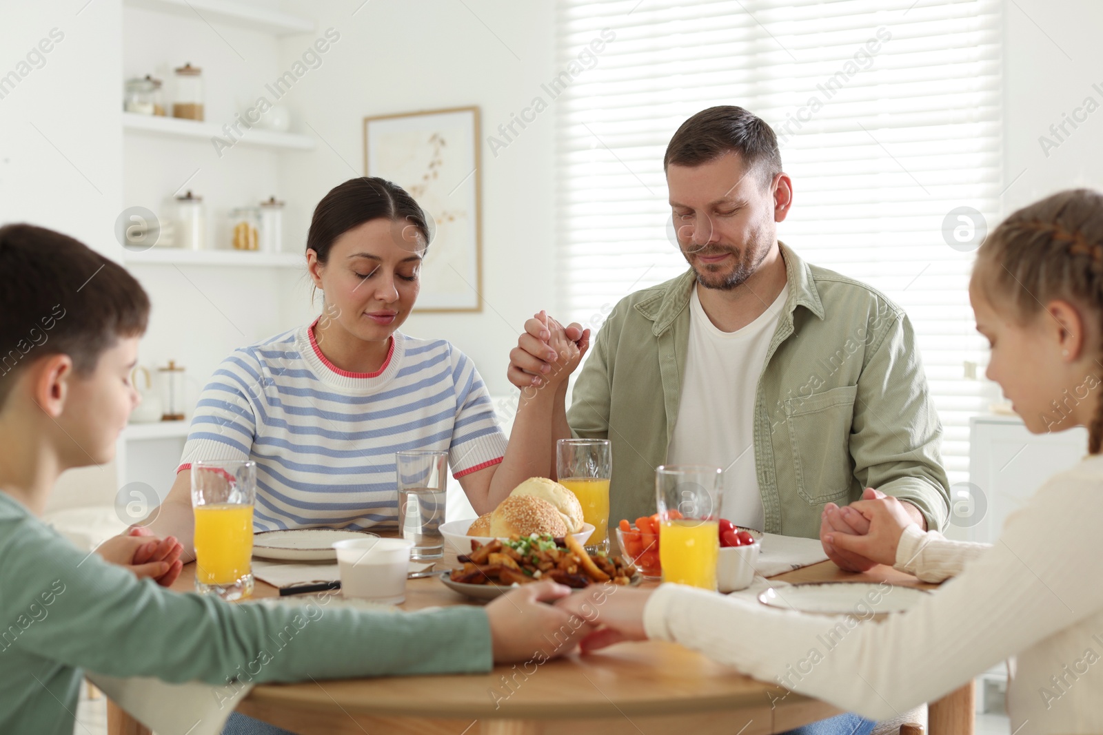 Family praying together before dinner at table indoors Photo of Family praying together before dinner at table indoors