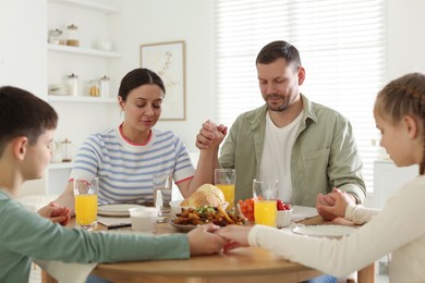 Photo of Family praying together before dinner at table indoors