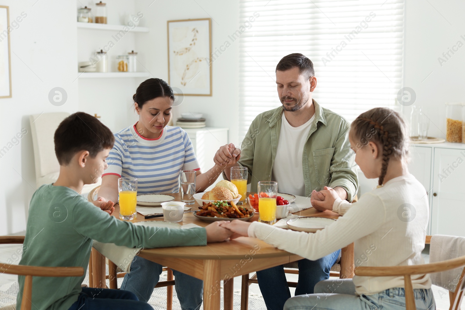 Family praying together before dinner at table indoors Photo of Family praying together before dinner at table indoors