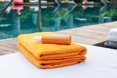 Photo of Beach towels and sunscreen on sun lounger near outdoor swimming pool. Luxury resort
