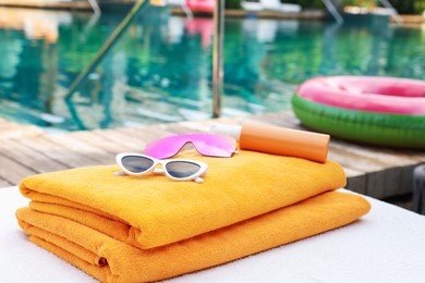 Photo of Beach towels and sunglasses on sun lounger near outdoor swimming pool. Luxury resort
