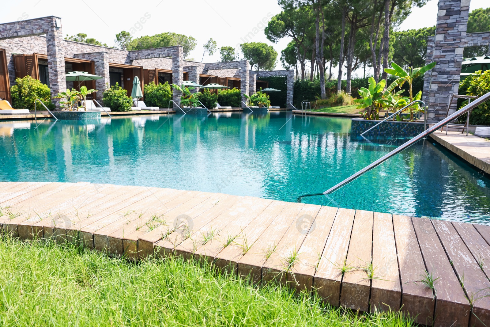Outdoor swimming pool with wooden deck, sunbeds and umbrellas at resort Photo of Outdoor swimming pool with wooden deck, sunbeds and umbrellas at resort